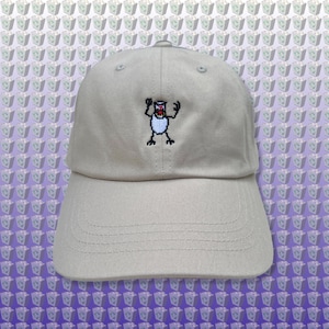 Pode incluir: Um boné de beisebol bege com um desenho de monstro de desenho animado bordado. O monstro é branco com olhos pretos e uma boca vermelha.