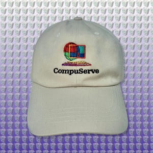 May include: A light beige baseball cap with the CompuServe logo embroidered on the front. The logo features a colourful globe, a computer screen, and the word "CompuServe" in black text. The cap has a curved peak.