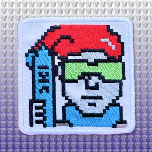 May include: A white embroidered patch with a pixelated image of a person wearing a red hat, green goggles, and a blue shirt. The person is holding a blue and white surfboard with the word "SURF" written on it.