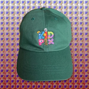 May include: A green baseball cap with an embroidered logo that says "Kid Pix" in colorful, pixelated letters.