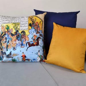 May include: Four decorative throw pillows on a gray couch. One pillow features a colorful illustration with figures and text. The other pillows are solid in navy blue and mustard yellow. The pillows add a decorative touch to any living space.