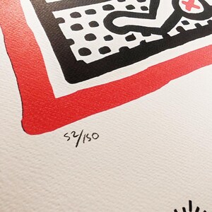 May include: A black and white print with a red border. The print features a black and white design with a red cross. The print is numbered 52/150.