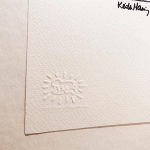 May include: A white paper with a black and white embossed stamp of a cartoon figure with a sun around it. The text "Keith Haring Foundation" is written in black ink in the upper right corner.