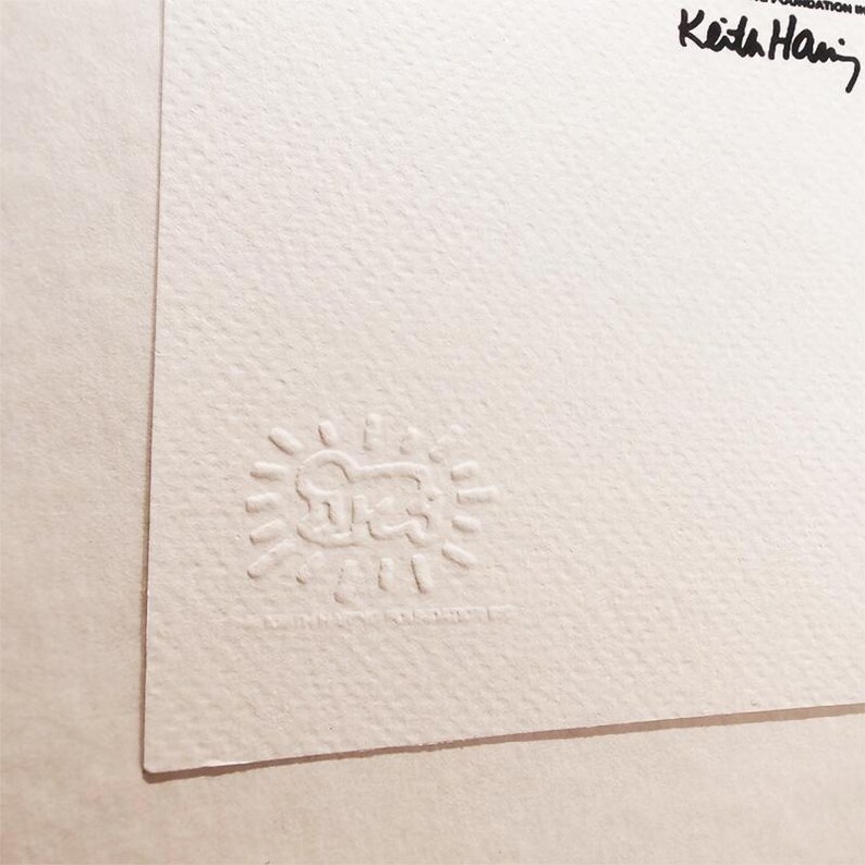 May include: A white paper with a black and white embossed stamp of a cartoon figure with a sun around it. The text "Keith Haring Foundation" is written in black ink in the upper right corner.