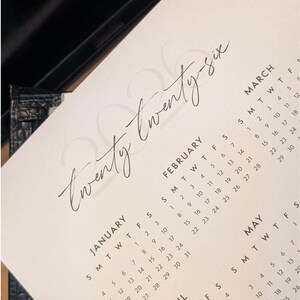 A printable 2026 calendar with a handwritten style date resting on a desk.