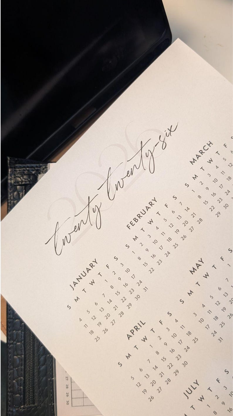 A printable 2026 calendar with a handwritten style date resting on a desk.