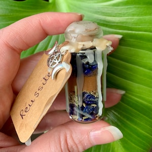 Peut inclure: Une petite bouteille en verre remplie de cristaux bleus et bruns, d'herbes et d'une bougie blanche. La bouteille est scellée à la cire et porte une étiquette qui dit "Réussite".