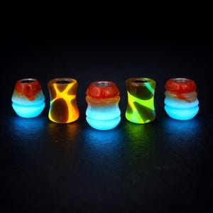 Peut inclure: Cinq bouchons décoratifs brillants. Chaque bouchon présente un design unique avec des couleurs telles que le rouge, l'orange, le jaune et le vert. Le bas de chaque bouchon brille d'une couleur bleu vif.