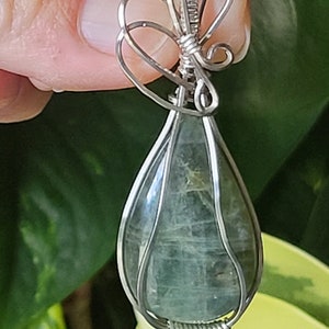 May include: A teardrop-shaped green gemstone pendant wrapped in silver wire with a decorative silver wire bow at the top.