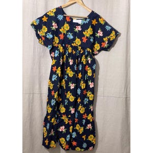 May include: A navy blue dress with a floral pattern featuring yellow, pink, orange, and blue flowers. The dress has short sleeves, a gathered waist, and a ruffled hem. It is hanging on a wooden hanger.