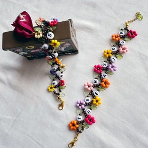 May include: Two beaded bracelets with colorful flower charms and the words "Together" and "Our Hearts" spelled out in white letters.