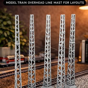 Puede incluir: Cinco mástiles grises de línea aérea para trenes modelo, diseñados para maquetas a escala HO. El texto de la imagen dice "5x HO Electric Railway Pole 1:87" y "MODEL TRAIN OVERHEAD LINE MAST FOR LAYOUTS". Los mástiles están sobre una vía de tren modelo.