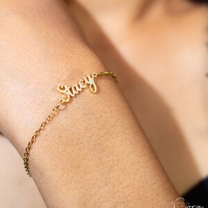May include: Gold name bracelet with the name "Stacy" in cursive lettering.