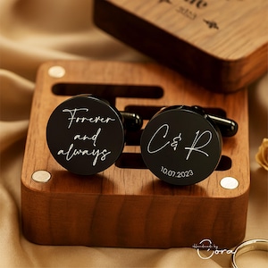 May include: Black round cufflinks with the words "Forever and always" and initials with a date in white script. The cufflinks are displayed in a wooden box with a matching lid.