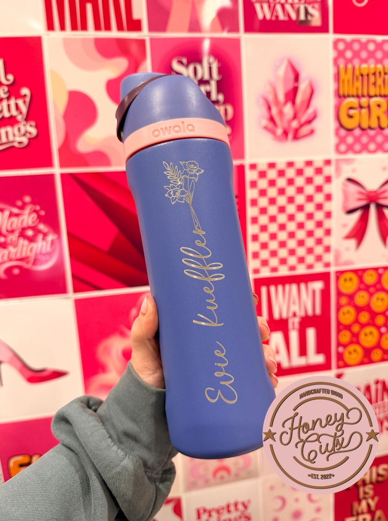 Puede incluir: Una botella de agua Owala azul con asa y detalles en rosa claro. La botella est&aacute; grabada con un dise&ntilde;o floral y el nombre "Evie Kueffler". El fondo presenta un collage de im&aacute;genes rosas y rojas.