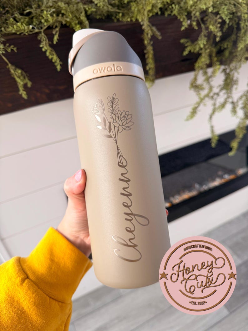 May include: A beige Owala water bottle with a floral design and the name "Cheyenne" engraved on the side. The bottle has a gray and white lid. The Honey Cute logo is visible in the bottom right corner.