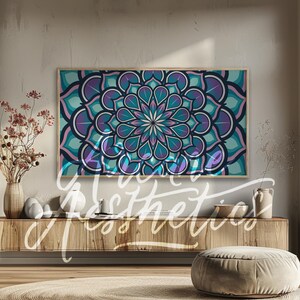 May include: A teal, purple, and pink mandala design with a white center. The mandala is framed and hanging on a wall above a wooden shelf.