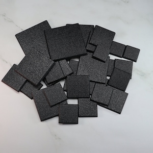 May include: A pile of black square-shaped foam tiles. The tiles are various sizes and are stacked on top of each other.