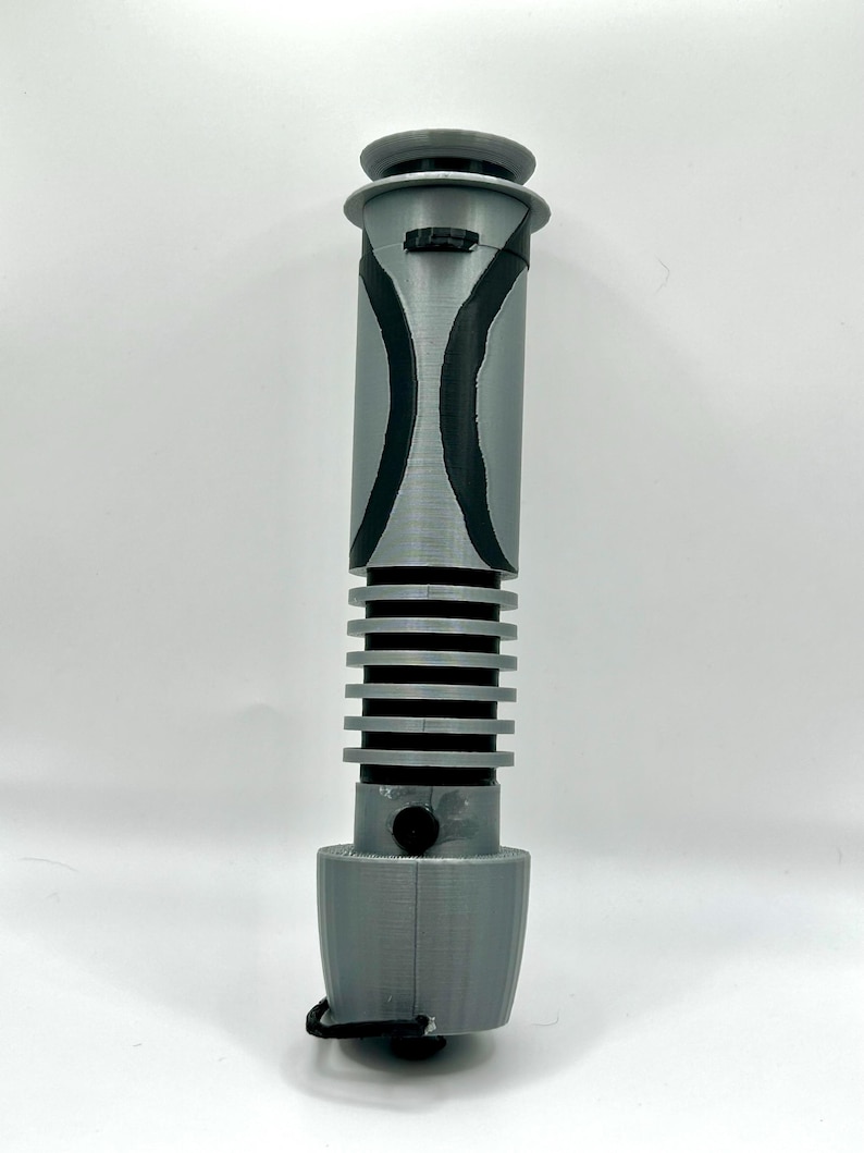 Peut inclure: Une r&eacute;plique de sabre laser gris et noir avec une poign&eacute;e stri&eacute;e et un motif noir et gris sur la poign&eacute;e.