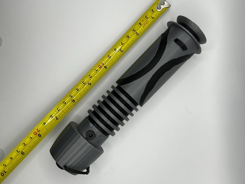 Peut inclure: Une poign&eacute;e de sabre laser grise avec une poign&eacute;e noire et une section nervur&eacute;e. La poign&eacute;e mesure environ 28 cm de long.
