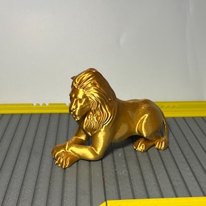 May include: A golden lion figurine in a resting pose. The sculpture has detailed features, including a flowing mane and paws. The lion is a decorative item, possibly a home decor piece.