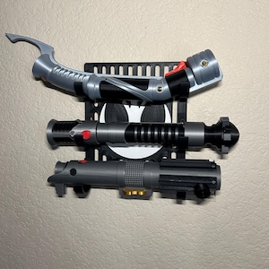 May include: A black wall mount holding three lightsabers. The lightsabers are gray and black with red and gold accents. The wall mount has a Batman logo in the center.