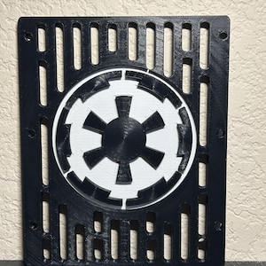 May include: Black and white 3D-printed wall art featuring the Galactic Empire symbol. The symbol is centered within a rectangular frame with vertical cutouts. The design is a fan-made item.