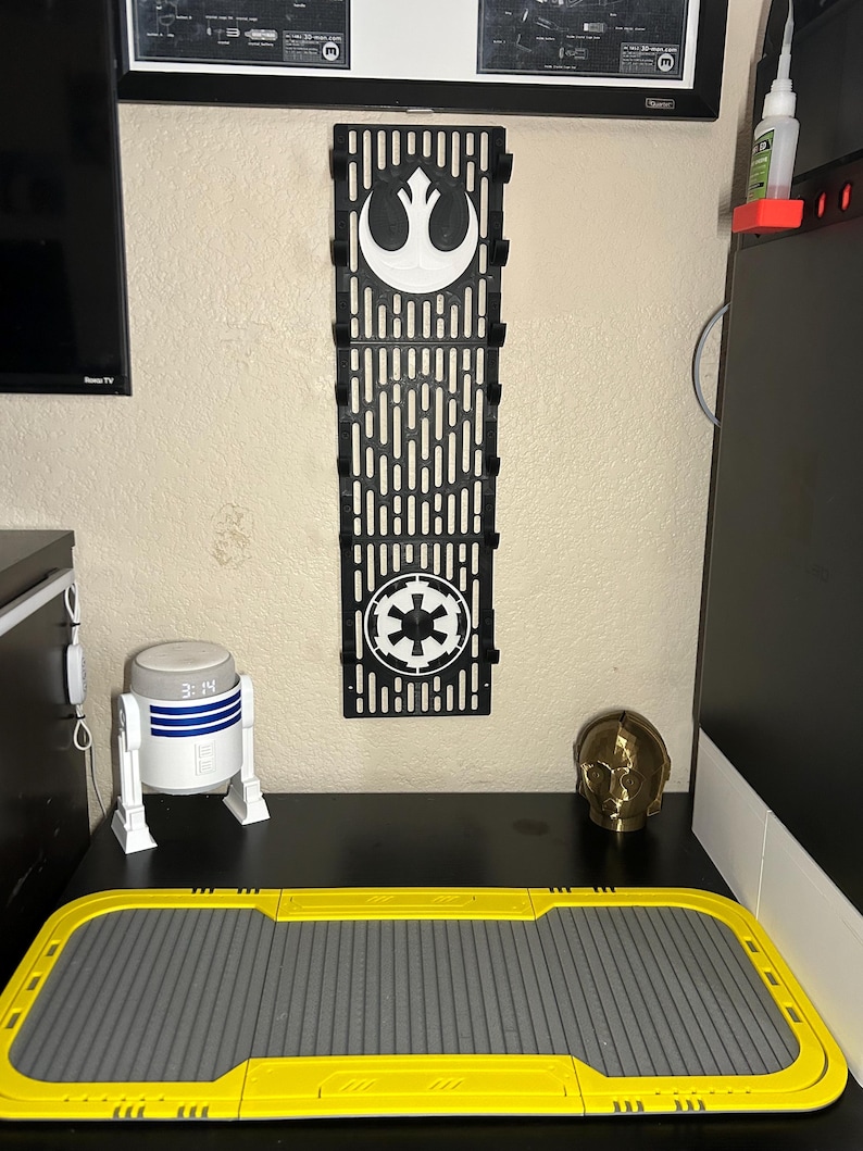 May include: A black wall organizer featuring the Rebel Alliance and Galactic Empire symbols. A white and blue R2-D2 clock, a gold C-3PO head, and a yellow and gray tray are on a black surface.
