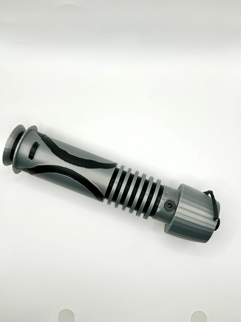 Peut inclure: Un accessoire de sabre laser gris avec des accents noirs et une surface textur&eacute;e. Le sabre laser a un cordon noir attach&eacute; &agrave; l'extr&eacute;mit&eacute;.