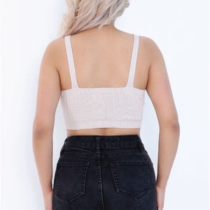 May include: A beige knitted crop top with thin straps and a square neckline. The top is worn with black denim shorts.