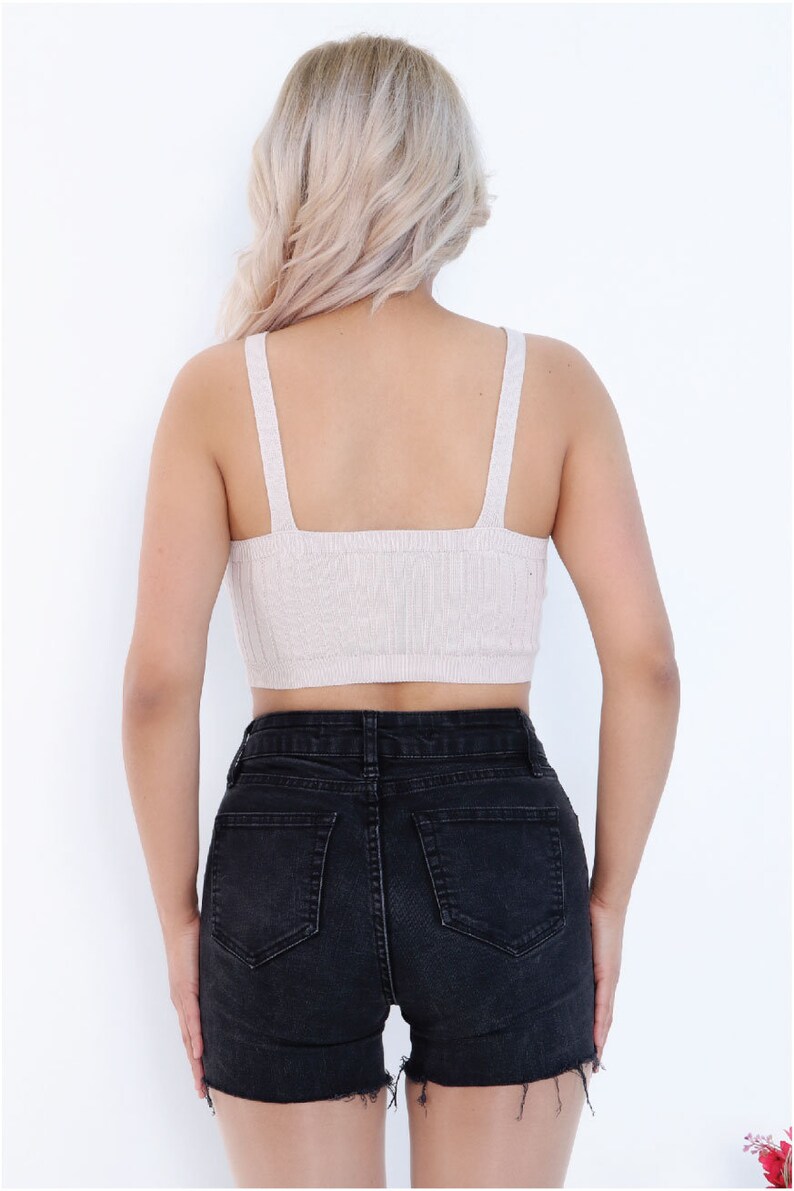 May include: A beige knitted crop top with thin straps and a square neckline. The top is worn with black denim shorts.