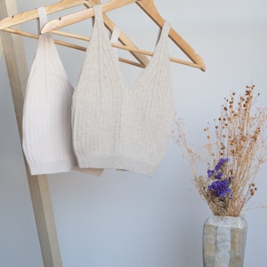 May include: Two beige ribbed tank tops hanging on wooden hangers with the word "BEJE" printed on the hangers.