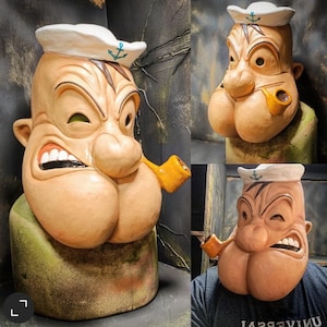 Puede incluir: Una escultura de cerámica de un marinero de dibujos animados con una nariz grande y una pipa. La escultura está pintada en tonos marrones y beige, con un sombrero de marinero blanco y un ancla azul.