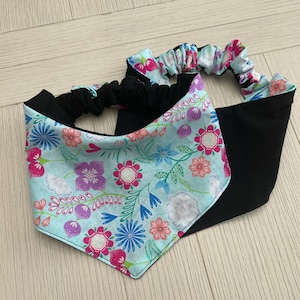 May include: A blue and black fabric headband with a floral pattern. The headband is made of two pieces of fabric, one black and one blue with a floral print. The headband is tied at the back of the head.