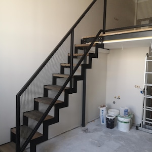 Może przedstawiać: Czarne metalowe schody z drewnianymi stopniami i balustradą z siatki. Schody prowadzą do antresoli.