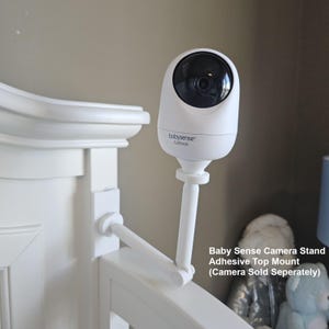 May include: A white Baby Sense camera stand with an adhesive top mount, attached to a crib. The camera has a black lens and the text "babysense FullPeek". The stand is designed to hold a camera (sold separately).