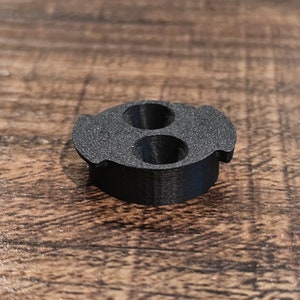 May include: Black plastic 3D printed part with two holes.