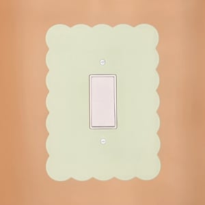 May include: A light green wall switch plate with a scalloped edge. The switch plate has a white light switch with two screws.