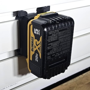 Puede incluir: Una batería DeWalt 20V Max XR Lithium Ion negra y amarilla con una capacidad de 5Ah está montada en una pared blanca.
