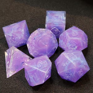 May include: Set of seven purple and white dice with swirling patterns. The dice are translucent and have a frosted finish.