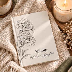 Może przedstawiać: Biały dziennik w twardej oprawie z czarną grafiką liniową przedstawiającą dwa goździki po lewej stronie. Tekst "Nicole" jest wydrukowany pogrubioną czcionką szeryfową nad napisem "Letters to my Daugther" na przedniej okładce.