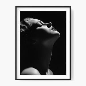 May include: Black and white framed print featuring a woman's profile, looking upwards with closed eyes. The image is dramatically lit, highlighting the face and neck against a dark background. The print is in a black frame.