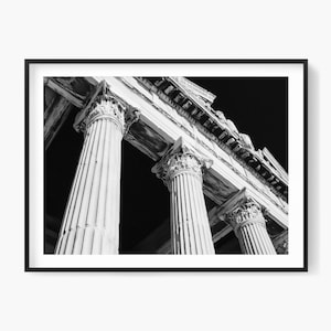 Op de afbeelding: Zwart-wit ingelijste print van oude Romeinse zuilen. De afbeelding is genomen vanuit een lage hoek, waardoor de hoogte en details van de zuilen en de architecturale structuur erboven worden benadrukt. De zuilen hebben gedetailleerde gravures.