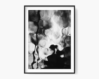 May include: Black and white abstract art print in a black frame. The image features a rippling water effect with light and dark areas, creating a textured appearance. The artwork is a modern, minimalist design.