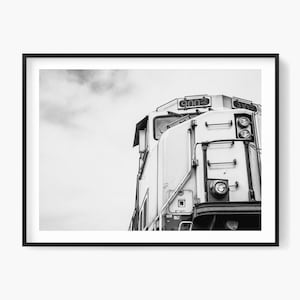 Puede incluir: Fotografía en blanco y negro de una locomotora. Se ve la parte delantera del tren, con faros, puertas y el número "900". El cielo es visible en el fondo.