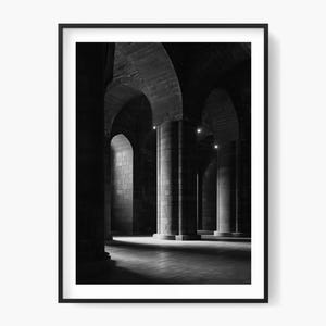 Könnte beinhalten: Schwarz-Weiß-Fotografie eines gewölbten Steinflurs mit großen Säulen. Das Bild ist in einem schwarzen Rahmen eingefasst. Die Beleuchtung erzeugt Schatten und hebt die architektonischen Details hervor.