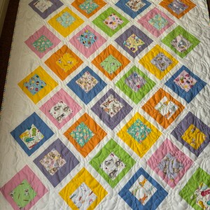 May include: A white quilt with a patchwork design featuring various pastel colored squares with different Easter-themed patterns. The quilt is quilted with a wavy pattern.