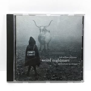 May include: A black and white CD case featuring a hooded figure with a satchel standing in a field facing a large long-horned bull. The text reads: hal willner presents weird nightmare meditations on mingus in a serif font.