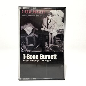 May include: A vintage cassette tape for T-Bone Burnett's album, "Proof Through The Night." The cassette case is black with the album title and artist's name in white. The cover art features a black and white photo of a man.