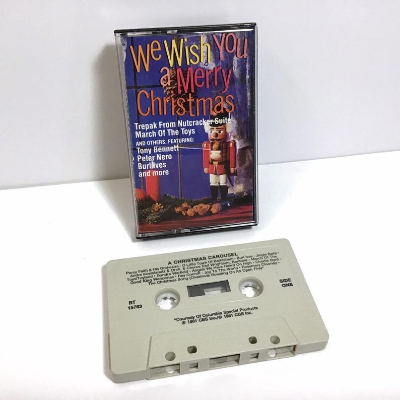 May include: A vintage cassette tape with a beige case and a label that reads "We Wish You a Merry Christmas." The label features a colorful illustration of a nutcracker and a Christmas tree. The cassette tape is titled "Trepak From Nutcracker Suite March Of The Toys" and features artists Tony Bennett, Peter Nero, Burlives, and more. The cassette tape is from 1981.